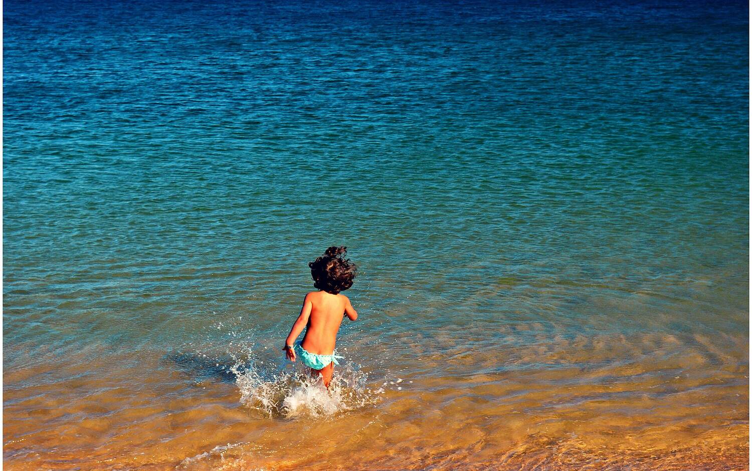 A child running into the clear water of an Algarve beach in Portugal